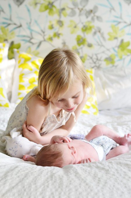 Big Sister Looking At Infant Baby Brother At Hands-on Newborn Photo Shoot