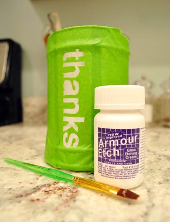 Glass etching cream and paintbrush next to glass jar with Hands-on tape stencil