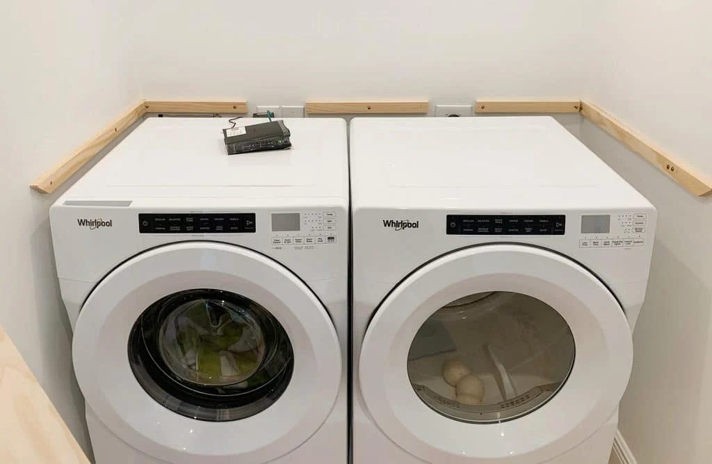Wood laundry shelf supports brought in to walls besides washer and dryer