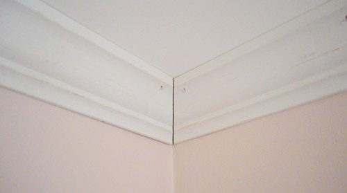 Corner of crown molding installed against ceiling with small seam at corner to be caulked