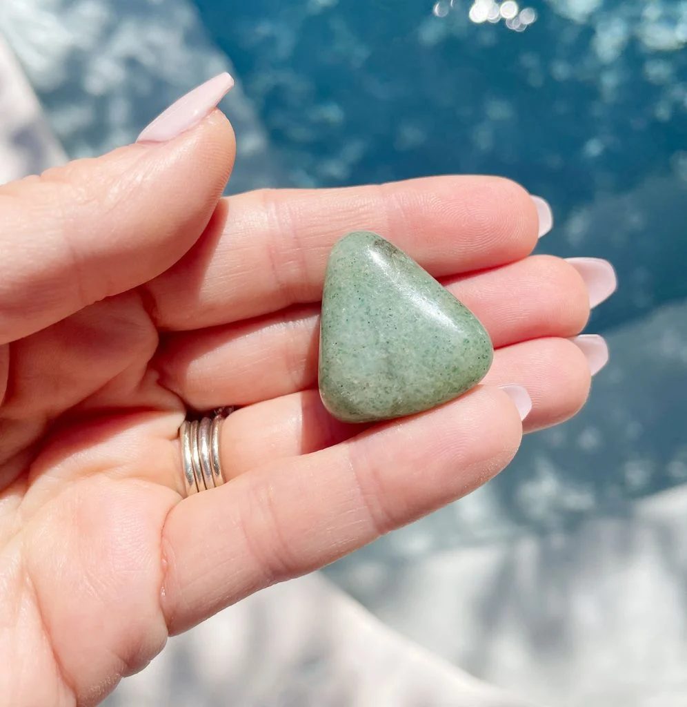 Hand holding green aventurine polished gemstone over water