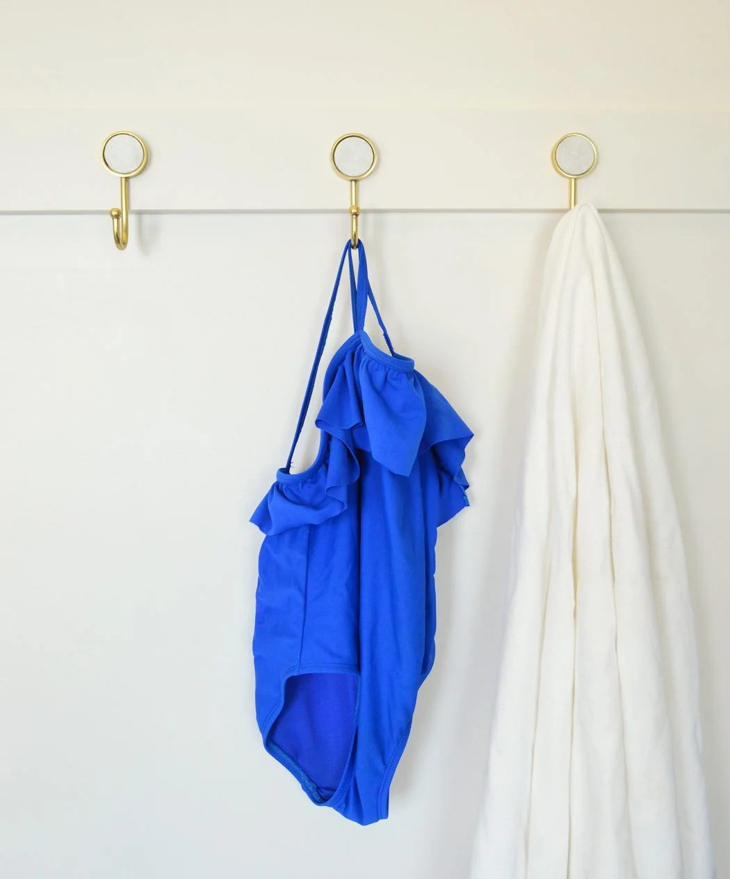 three gold hooks on hands-on rail with towel and bathing suit
