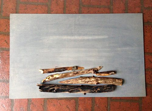 Cut tree branches stacked on gray stained plywood sheet for Hands-on holiday faux fireplace