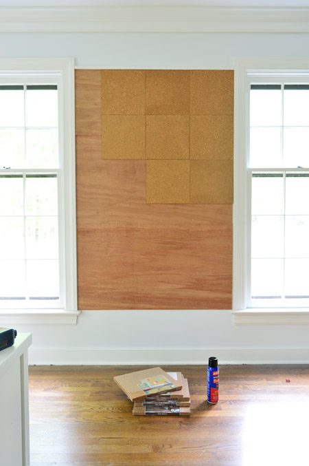 applying cork tiles to wall to create oversized cork board wall in kids art area