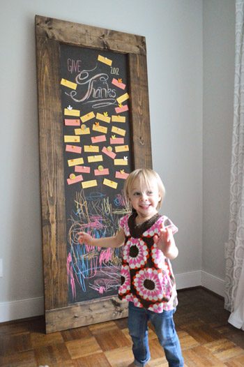 Toddler girl standing in front of Hands-on leaning chalkboard with Thanksgiving gratitude notes