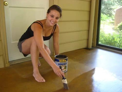 applying Behr Semi-Transparent Concrete Stain to concrete floor using a paintbrush