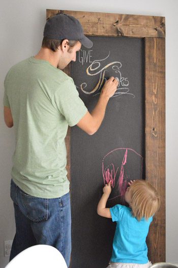 John and daughter both writing on large leaning Hands-on chalkboard with wood frame