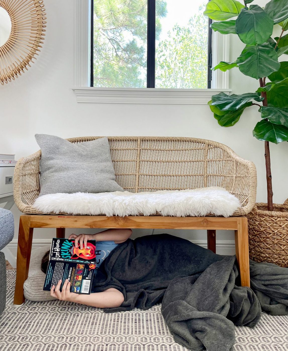 Kid Reading Under A Bench In Living Room With Blanket
