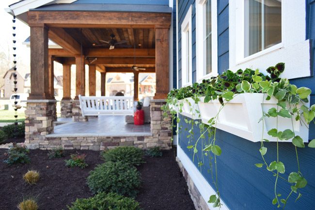 White Window Boxes Under Windows With Newburg Green Trim Next to Rustic Wood Porch