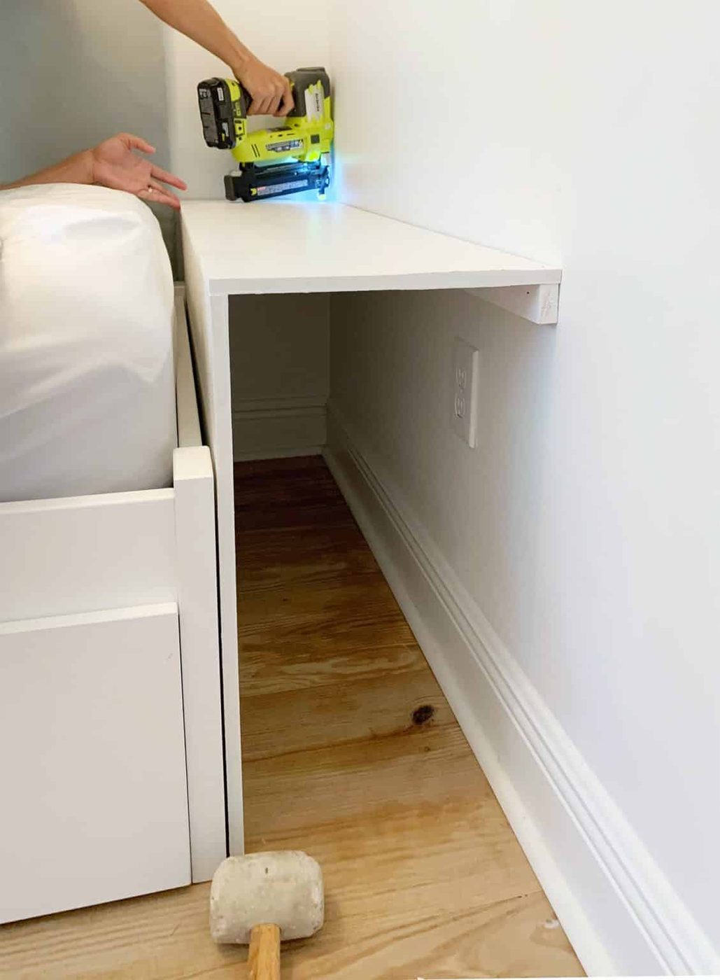 Painted pieces of MDF being nailed in for bottom shelf of built-in bookcase