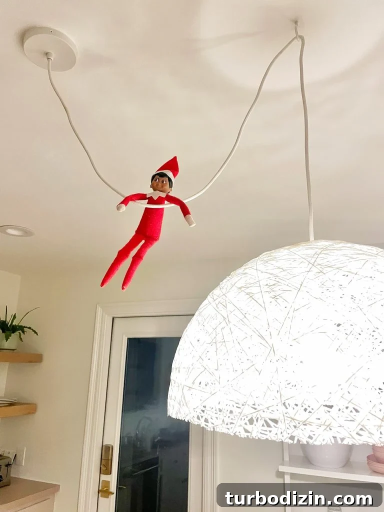 Elf on the Shelf hanging from pendant light cord in kitchen