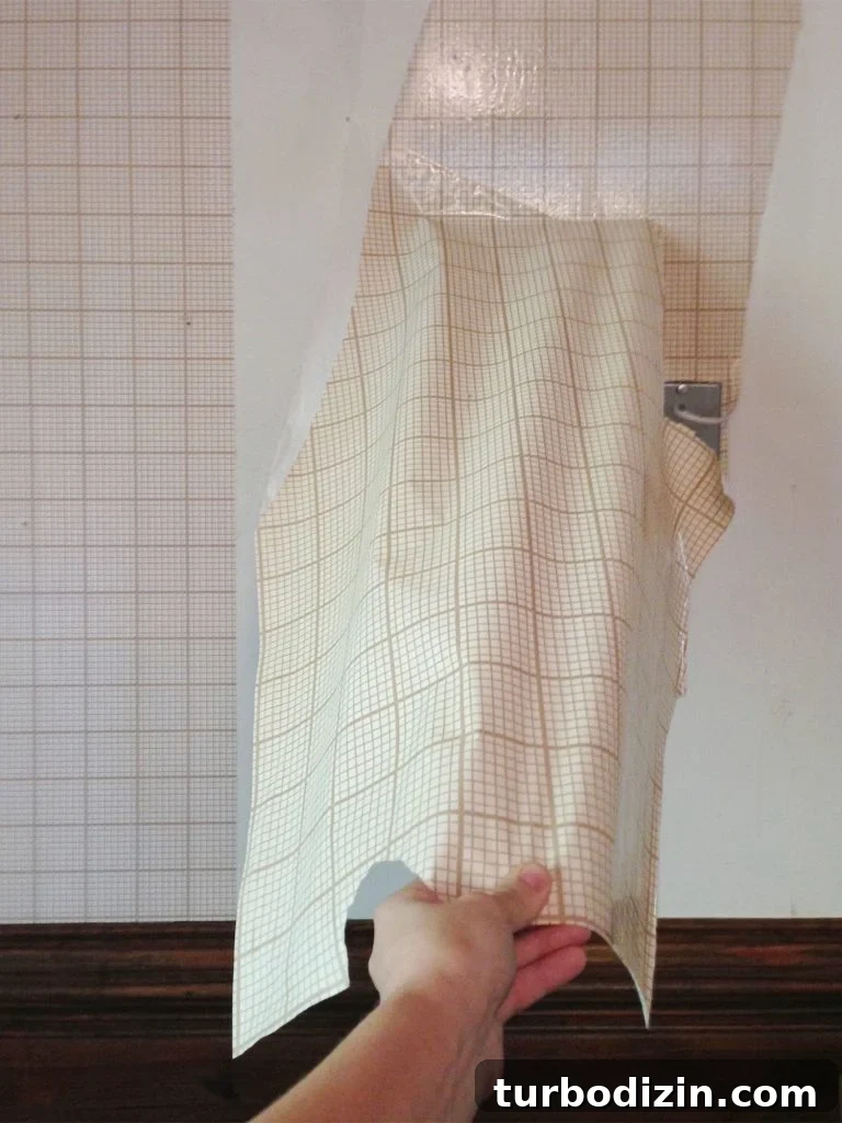 Hand peeling off large section of gridded wallpaper