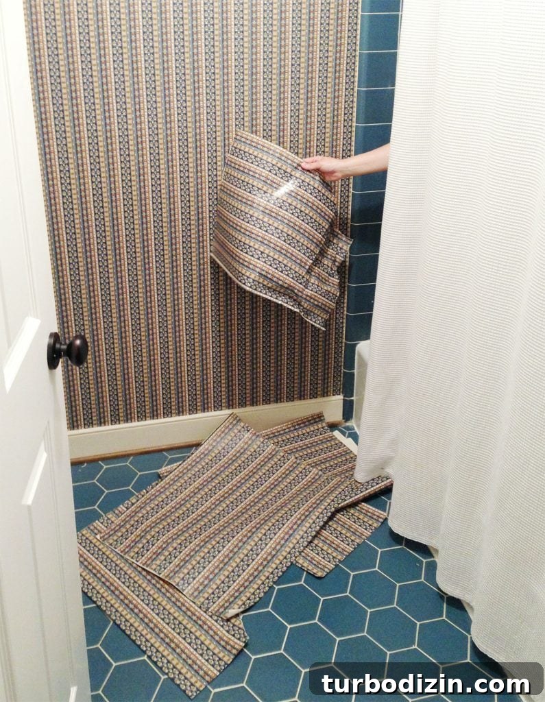 Hand removing wallpaper from shower in blue bathroom
