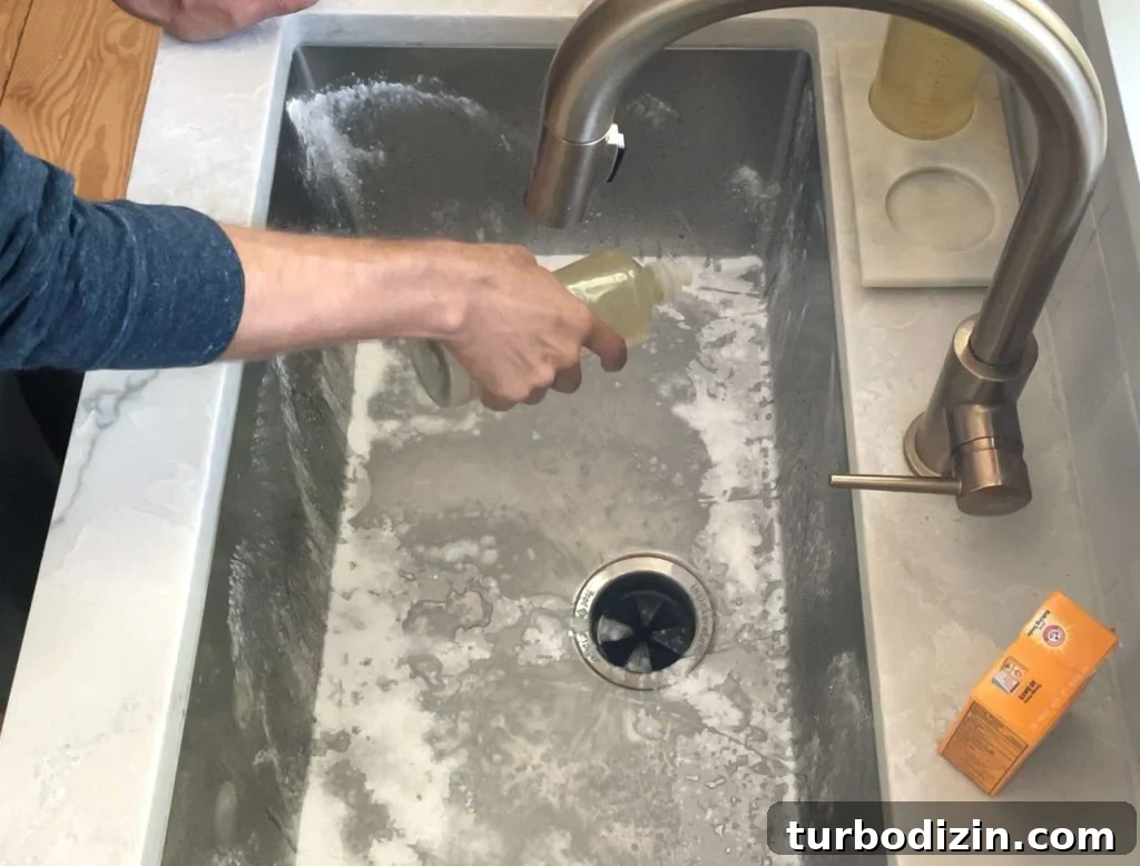 Hand squeezing dish soap into stainless steel sink covered with baking soda