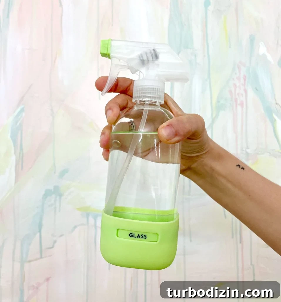 Homemade Window Cleaner Recipe for Streak-Free Glass 2 Hand Holding Homemade Window Cleaner In Glass Bottle In Front Of Colorful Painting