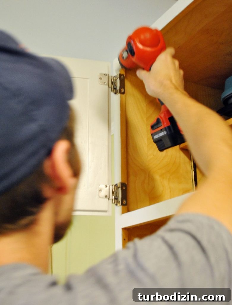 How to Paint Kitchen Cabinets Like a Pro: Step-by-Step Guide 13 John reattaching cabinet door in painted kitchen