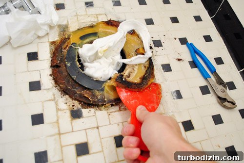Fix a Wobbly Toilet: Quick Steps to Stabilize It Safely 13 Scraping away old toilet wax ring with putty knife