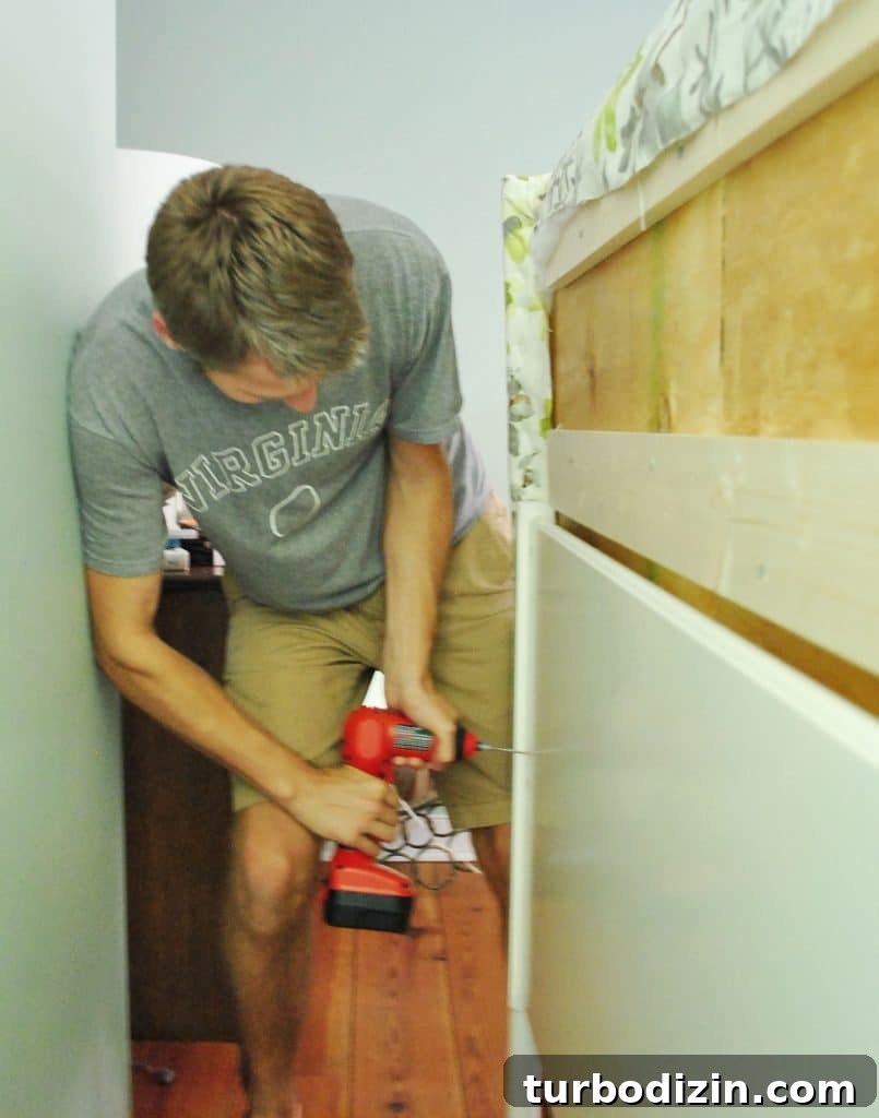John screwing DIY upholstered headboard onto frame from backside of bed