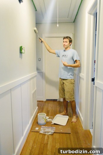 Board and Batten Wall Paneling for Under $60 17 painting a hallway gray with a paint roller using Benjamin Moore Nature Paint in Moonshine color