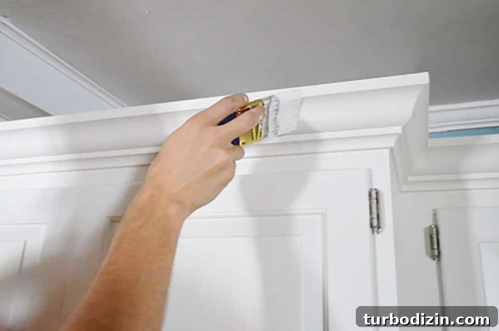 Add Crown Molding to Cabinets: Step-by-Step Guide for a Polished Finish 11 Painting crown molding on a kitchen cabinet with a short handled paint brush