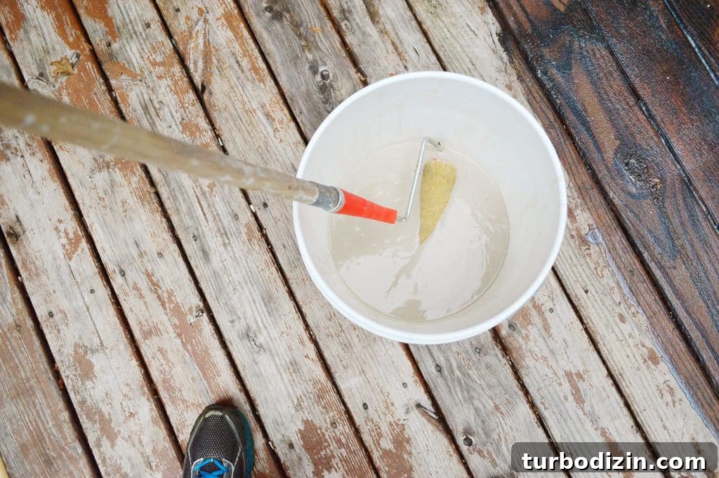 Dipping paint roller into bucket of deck stain stripper