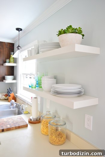 How We Installed Ikea Floating Shelves in Our Kitchen 2 two pairs of white Ikea LACK shelves hung in the kitchen with white plates, bowls, and colorful cups