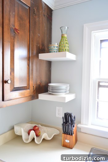 How We Installed Ikea Floating Shelves in Our Kitchen 16 two short Ikea floating shelves next to kitchen window holding stack of plates and carafe