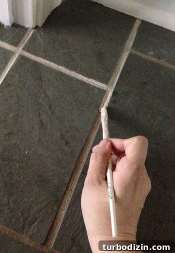 How We Restored Stained Grout to Bright White Again 9 applying Oyster Gray PolyBlend Grout Renew to dirty tile grout lines with paintbrush