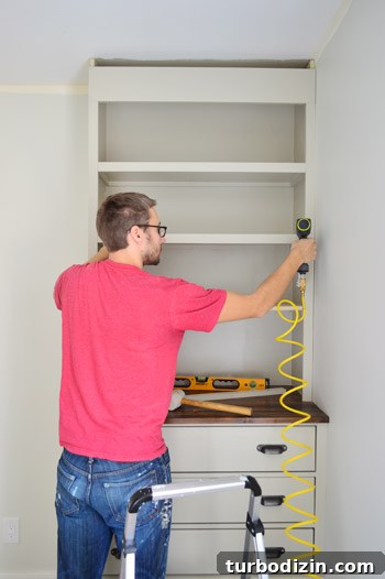 Man nailing trim pieces on the face of DIY bookshelf