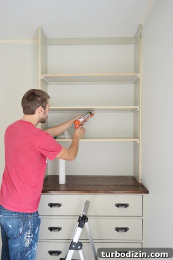 Man caulking under shelf of built in bookshelf