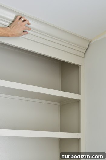 Hand holding crown molding piece in place on DIY bookshelf