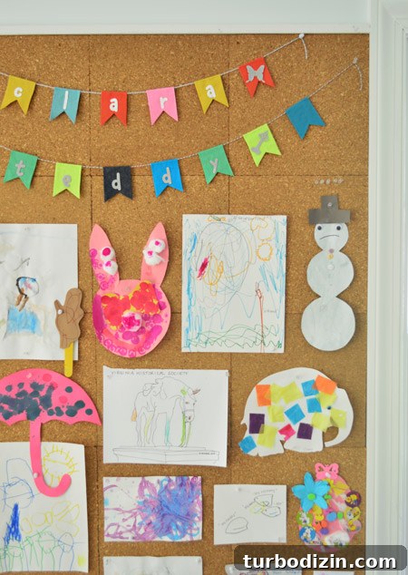Create a Cork Wall Gallery for Kids’ Artwork 14 close up detail of kids art hung on cork board wall including name banner bunting from etsy