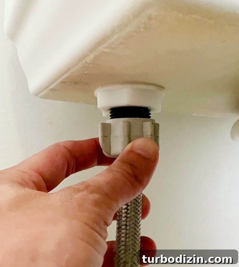 Hand Loosening Water Supply Line Under Toilet Tank