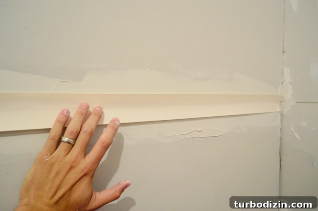 Drywall Taping, Mudding, and Sanding: Step-by-Step Guide 11 hand pushing drywall tape into bed of drywall mud along seam