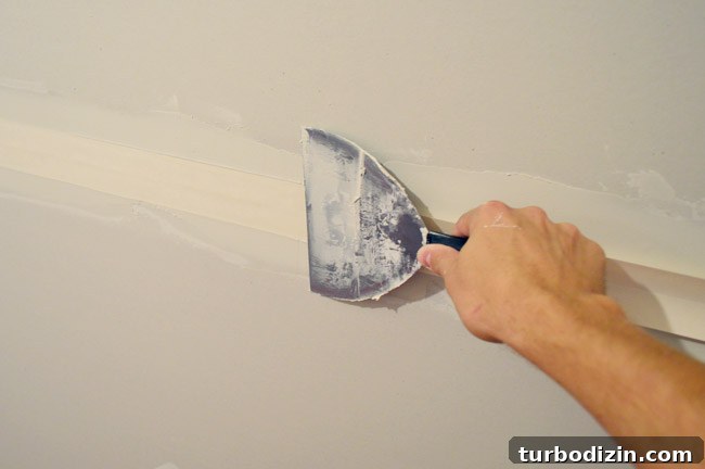 Drywall Taping, Mudding, and Sanding: Step-by-Step Guide 12 drywall knife smoothing tape into drywall tape and bottom layer of mud