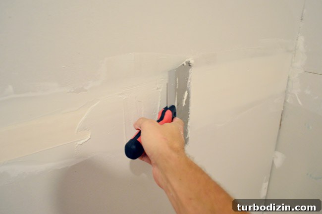 Drywall Taping, Mudding, and Sanding: Step-by-Step Guide 13 larger drywall knife being dragged across tape to apply another layer of mud