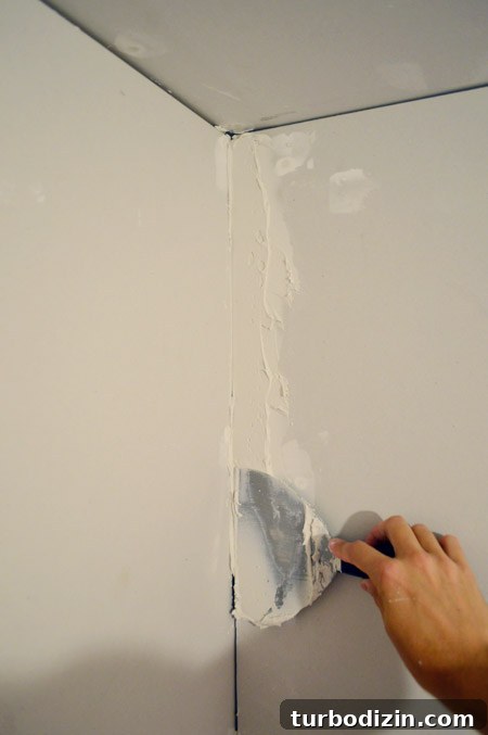Drywall Taping, Mudding, and Sanding: Step-by-Step Guide 16 flat drywall knife putting joint compound into corner of room