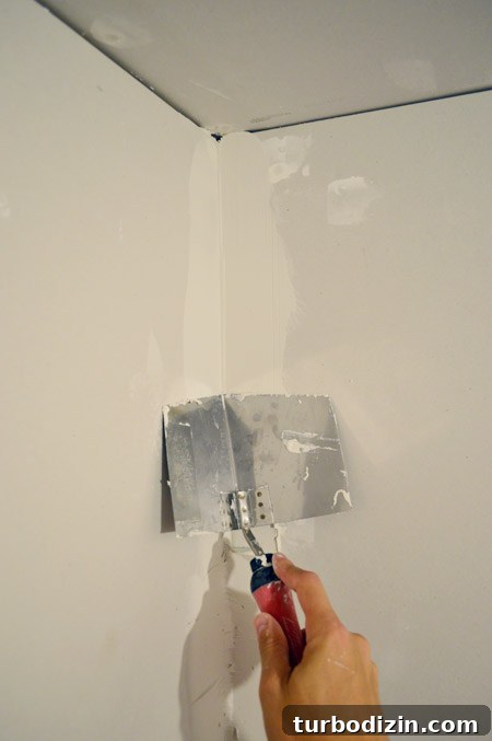 Drywall Taping, Mudding, and Sanding: Step-by-Step Guide 17 corner trowel smoothing thick first layer of drywall mud in room corner