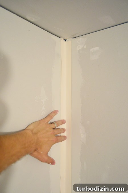 Drywall Taping, Mudding, and Sanding: Step-by-Step Guide 18 handing pressing drywall tape into corner layer of mud