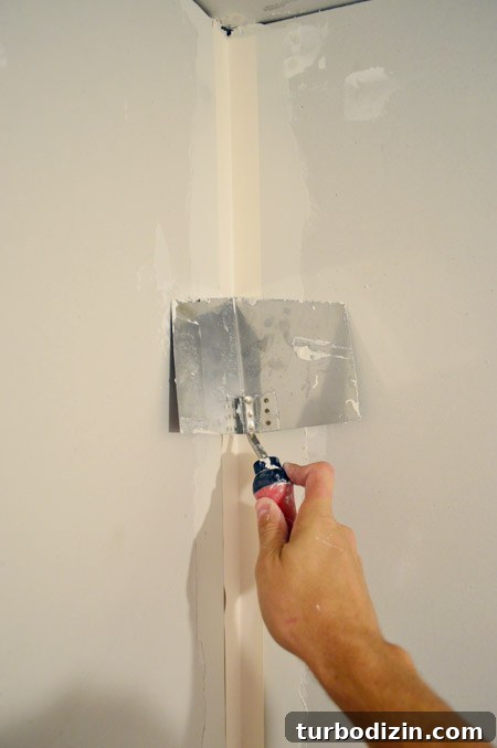 Drywall Taping, Mudding, and Sanding: Step-by-Step Guide 19 corner trowel pressing tape into corner of drywalled room