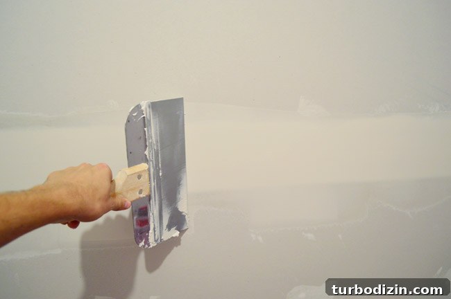 Drywall Taping, Mudding, and Sanding: Step-by-Step Guide 21 John dragging large drywall knife over seam in drywall to smooth mud