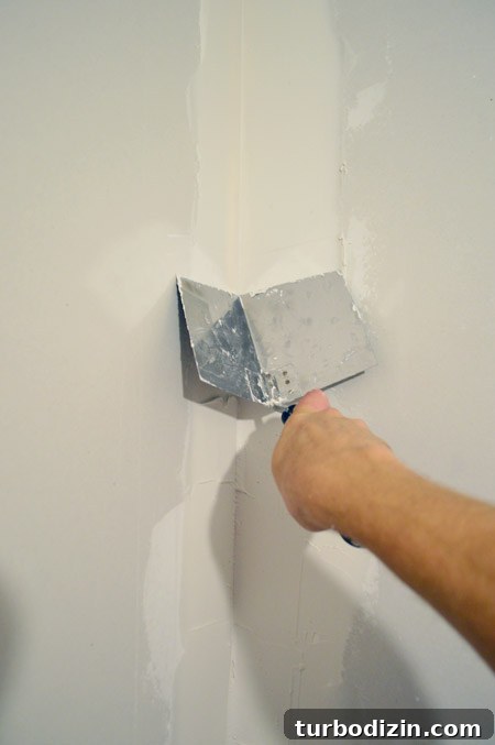 Drywall Taping, Mudding, and Sanding: Step-by-Step Guide 23 John smoothing drywall mud in corner of room using corner trowel