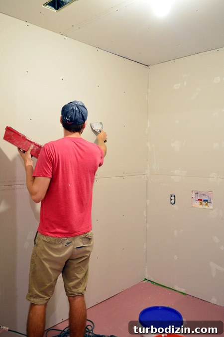 Drywall Taping, Mudding, and Sanding: Step-by-Step Guide 8 John applying mud over drywall screw head marks