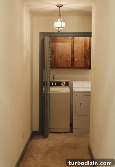 How We Transformed Our Bonus Room Into a Stylish Lounge 16 Dated laundry room closet at end of a hall with bifold doors, dark cabinets, carpet, and mismatched old washer and dryer