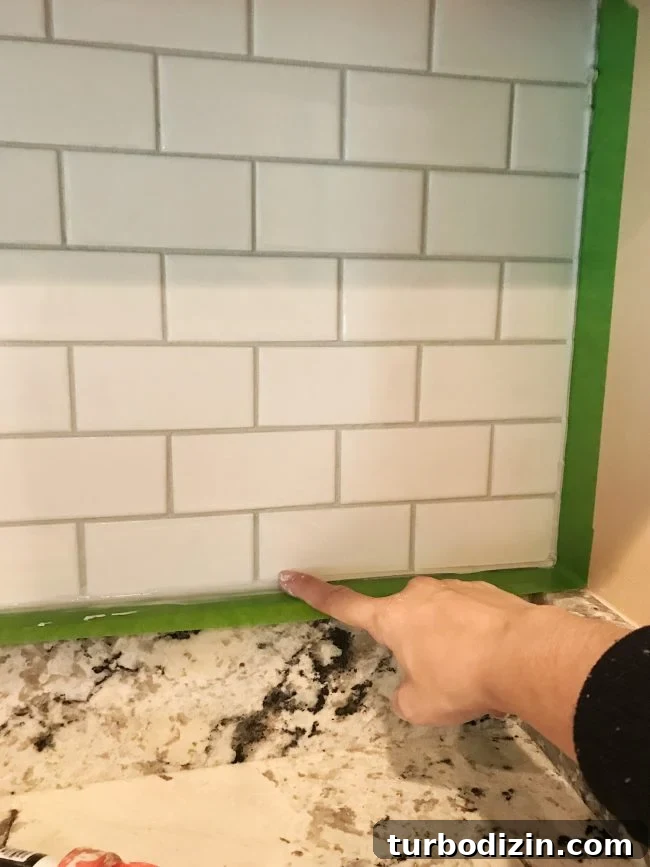 Install a Subway Tile Kitchen Backsplash for $200 DIY Guide 16 Sherry spreading caulk with finger along edges of installed backsplash