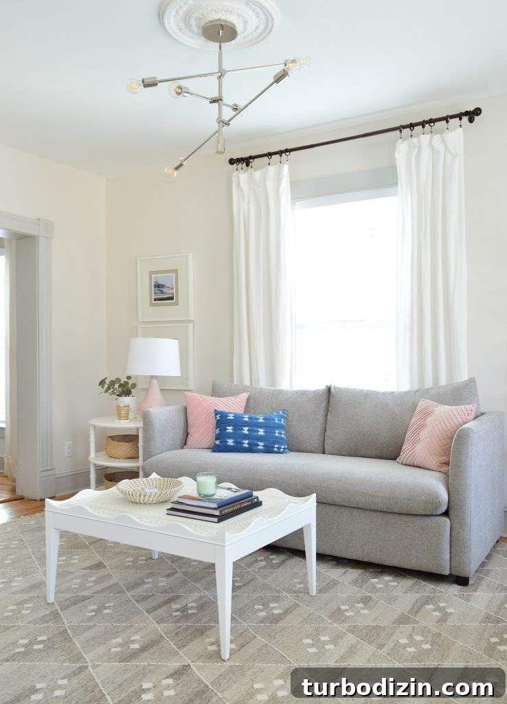 Bright, Airy Living Room Ideas That Stay Comfortable and Practical 3 bright neutral living room gray sofa with white scalloped coffee table and modern chandelier