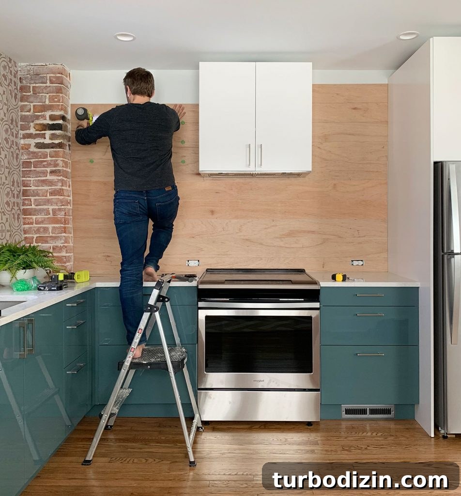 DIY Shiplap Wall Plank Makeover for $31 Total 20 John Standing On Ladder Nailing Wood Paneled Backsplash In Blue Kitchen