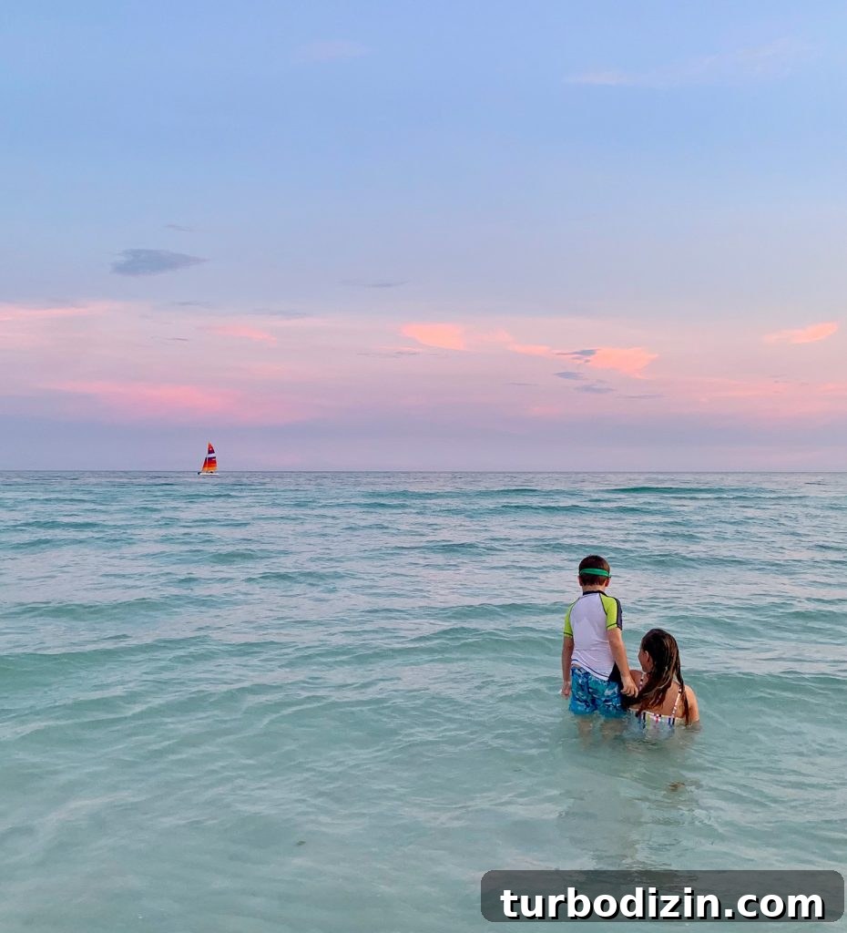 Kids playing in Gulf of Mexico at sunset with sailboat in background