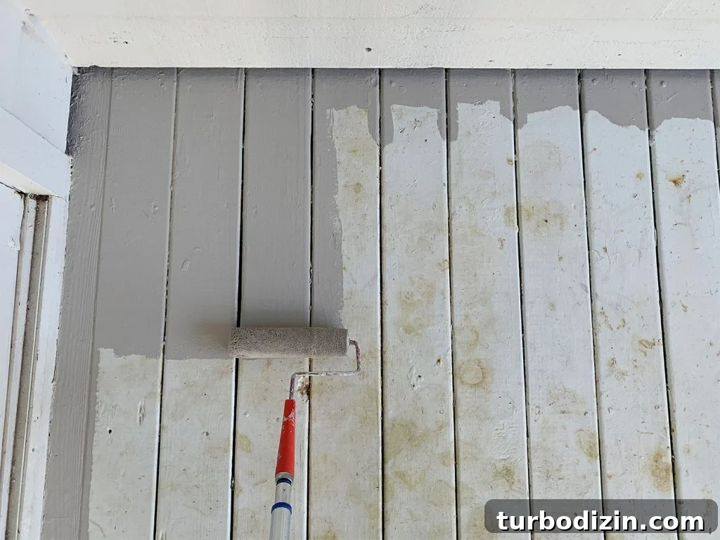 Roller applying gray porch paint to stained white porch floor