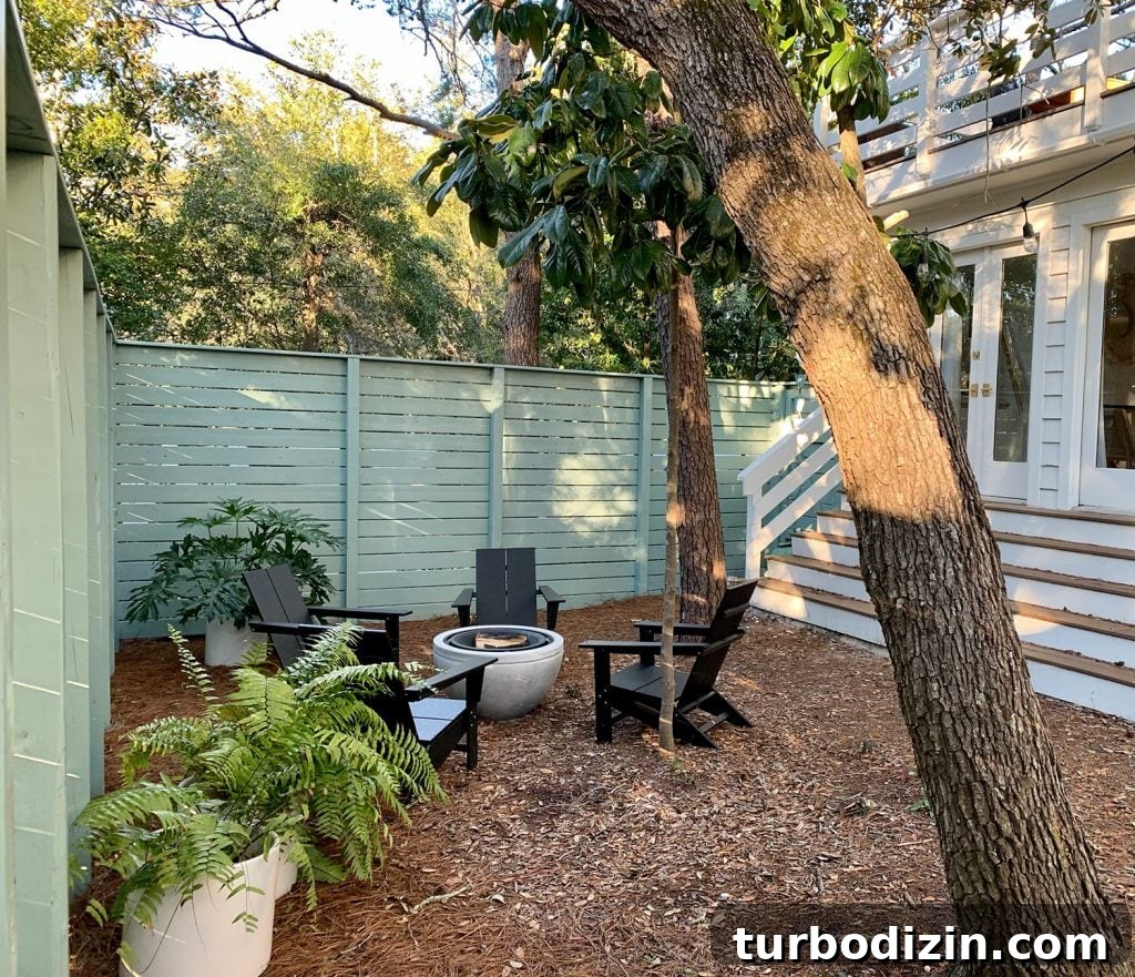 Green fenced side yard with black Adirondack chairs around fire pit